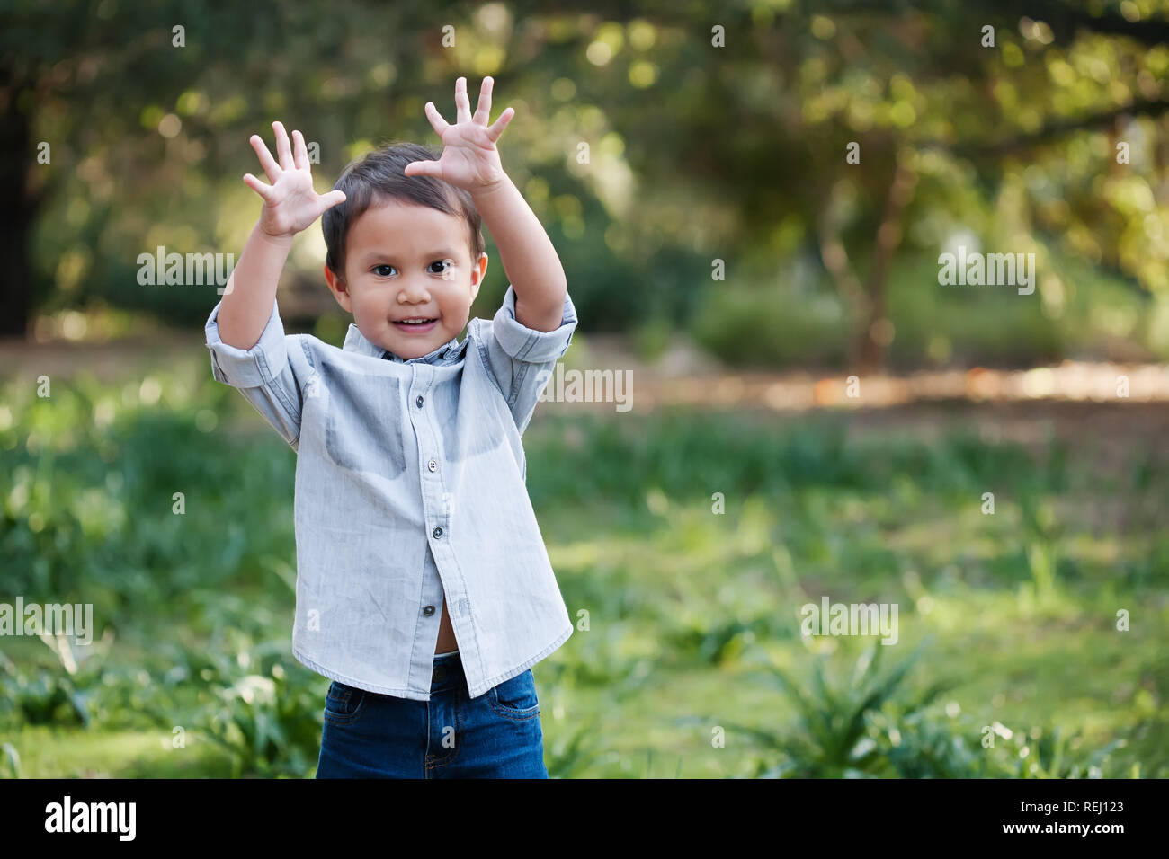 Young toddler boy using his hands to express himself, standing outdoors in a green field looking happy. Stock Photo