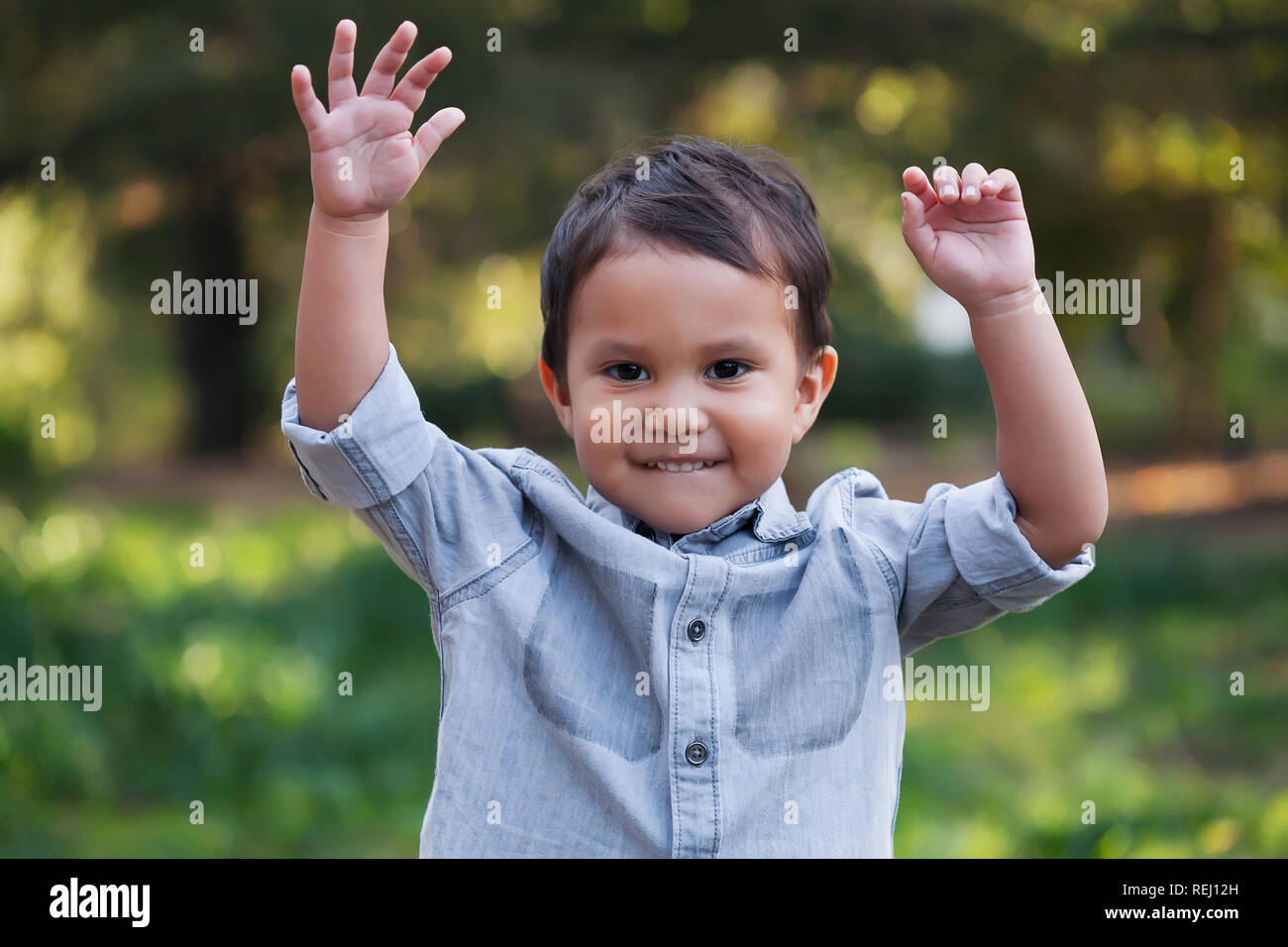 A handsome young boy, nicely dressed showing an expression of joy with hands up in the air looking excited and happy to be playing outdoors. Stock Photo