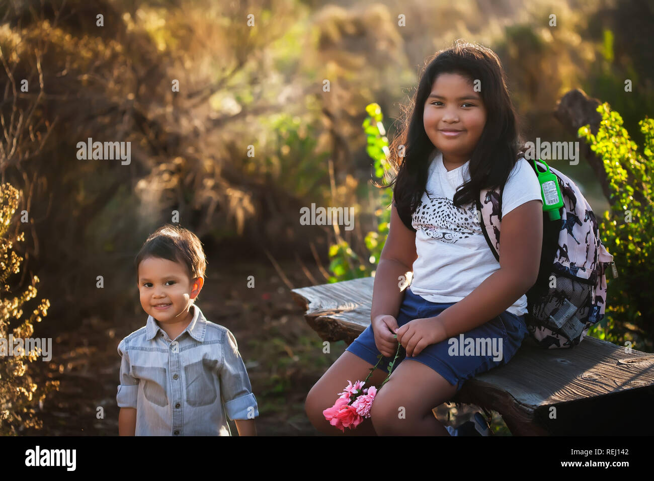 A boy and his older sister are sitting down, taking a break during a hike or field trip while the sun is setting. Stock Photo