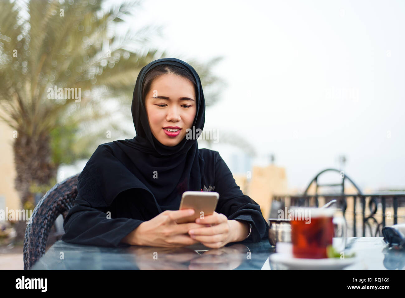 Muslim woman using phone while having a cup of coffee outdoors Stock Photo