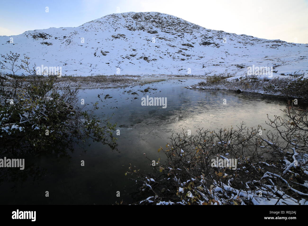 Small Lake Under A Mountain Peak Covered In Snow In Late Autumn Stock Photo