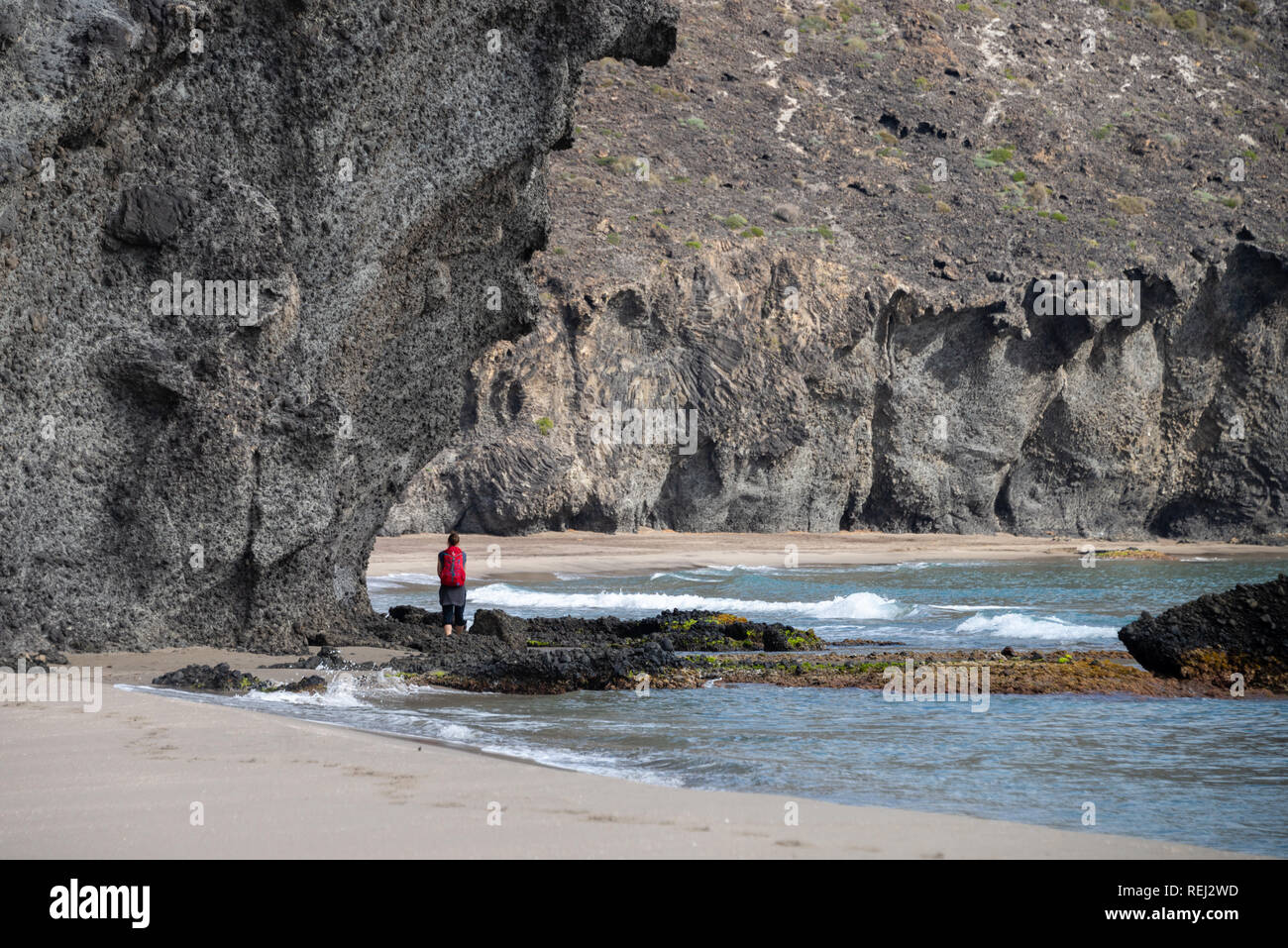 Female hiker walking pass volcanic rocks on the beaches of Cabo de Gata Natural Park,  Andalusia, Spain Stock Photo