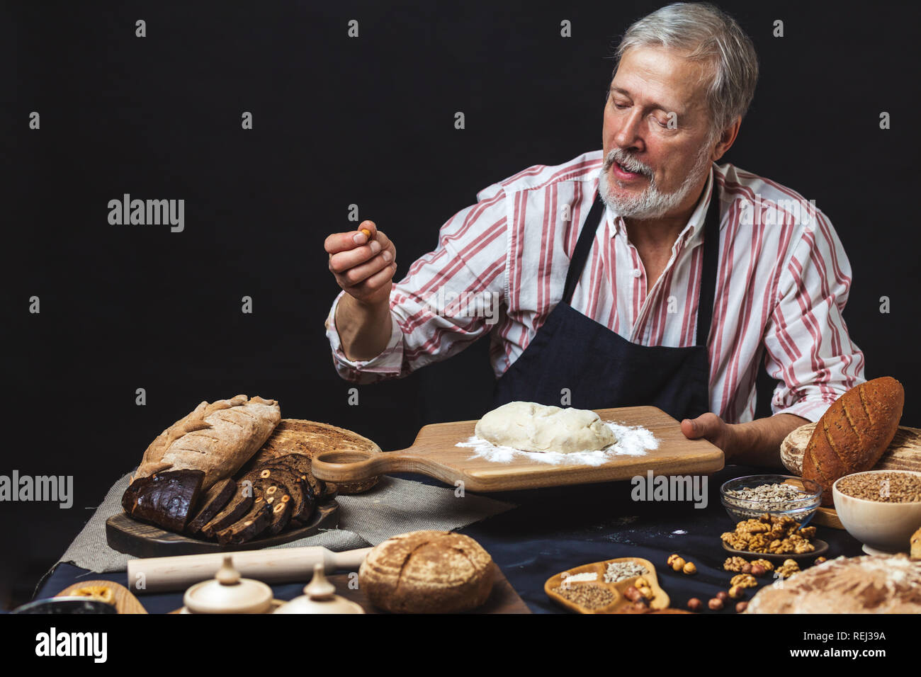 Mature bearded baker man kneading dough for bread on table Stock Photo