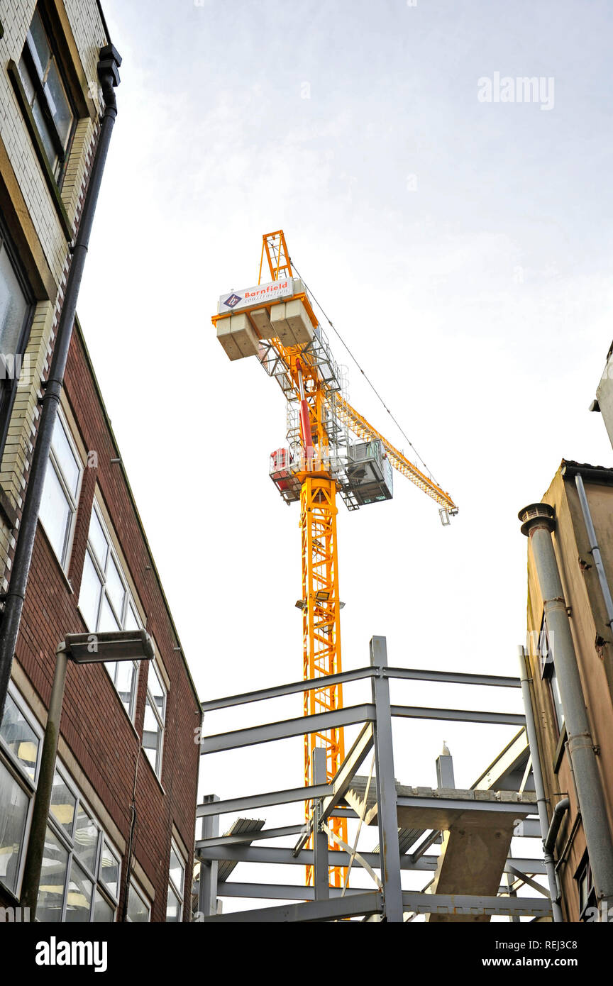 Large yellow tower crane viewed from oblique angle between old buildings Stock Photo