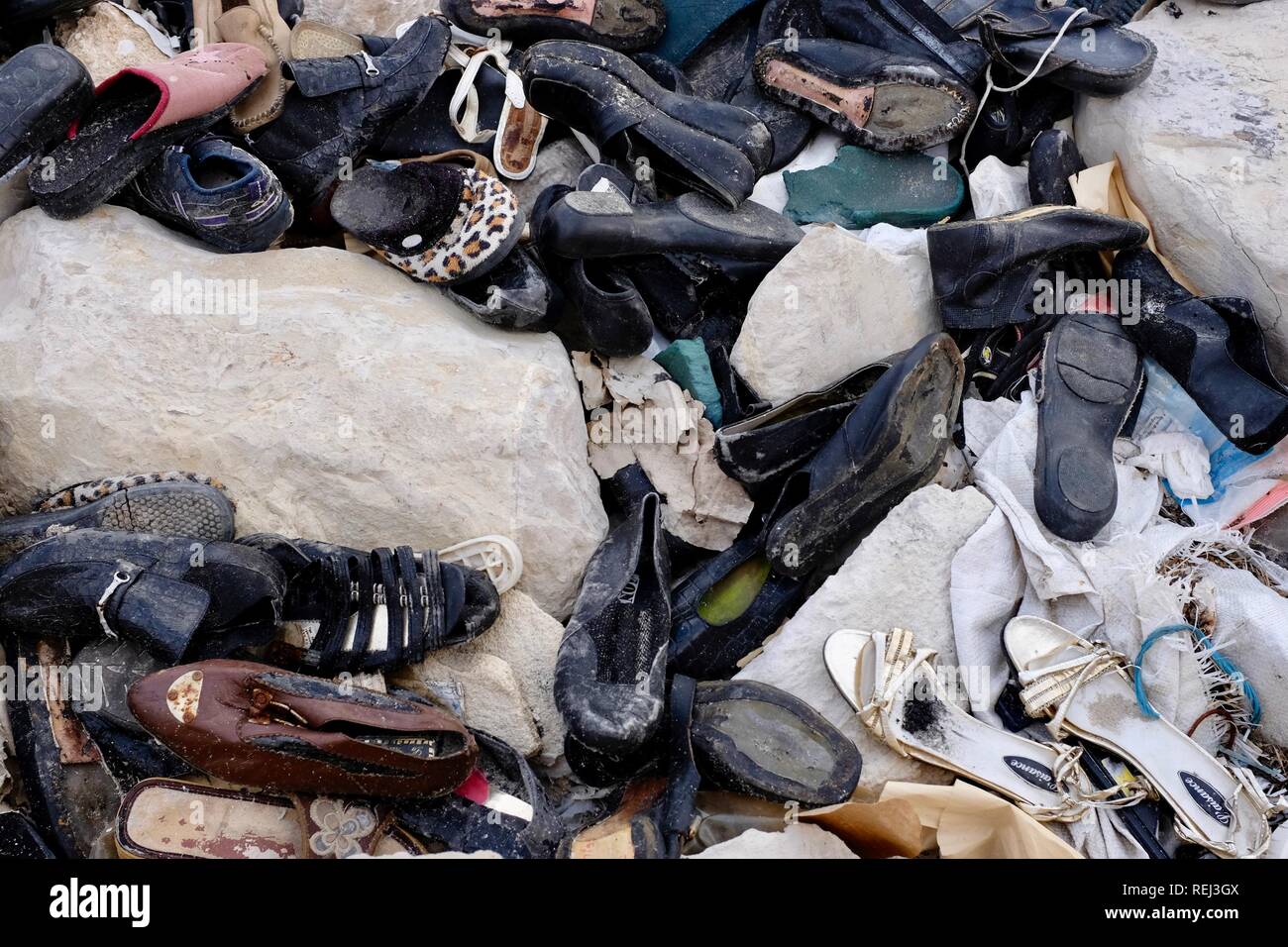 A pile old shoes and plastic dumped on the rocks on the coast Stock Photo
