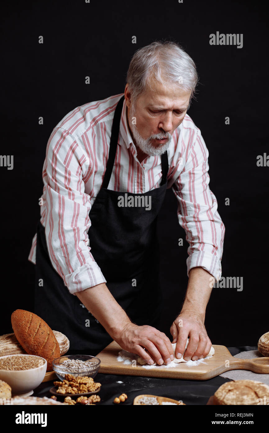 Mature bearded baker man kneading dough for bread on table Stock Photo