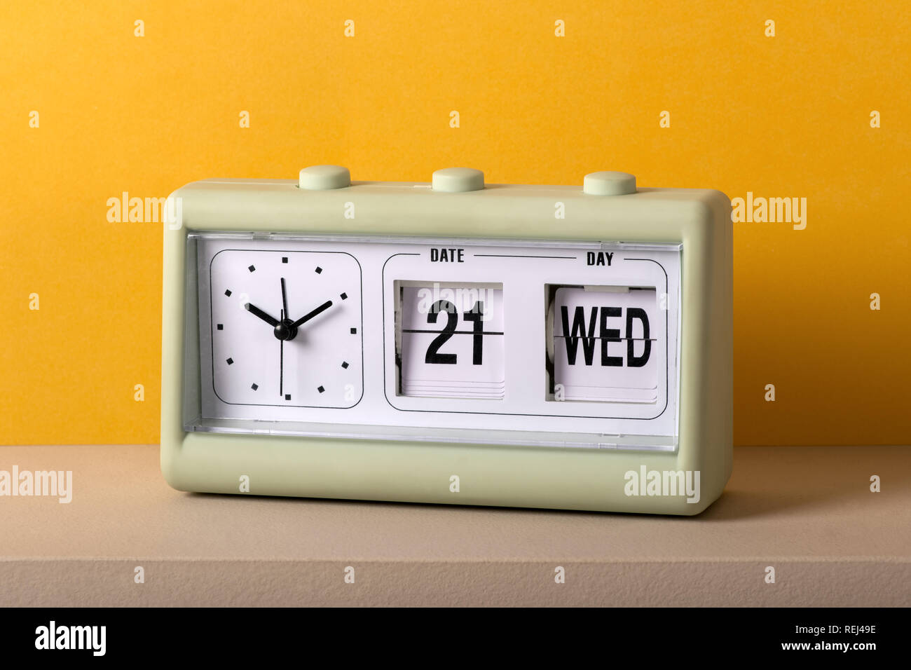 Vintage plastic tabletop clock with date, including the day in large numbers, and the time on a white dial without numerals against a colorful yellow  Stock Photo