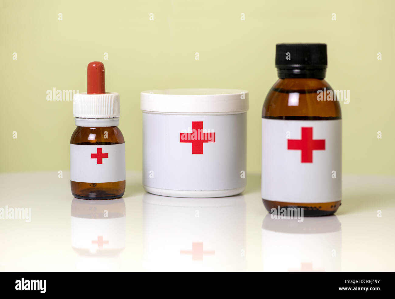 Three assorted medicine containers for dispensing medication with a dropper bottle, plastic tub and brown glass bottle labelled with red crosses Stock Photo