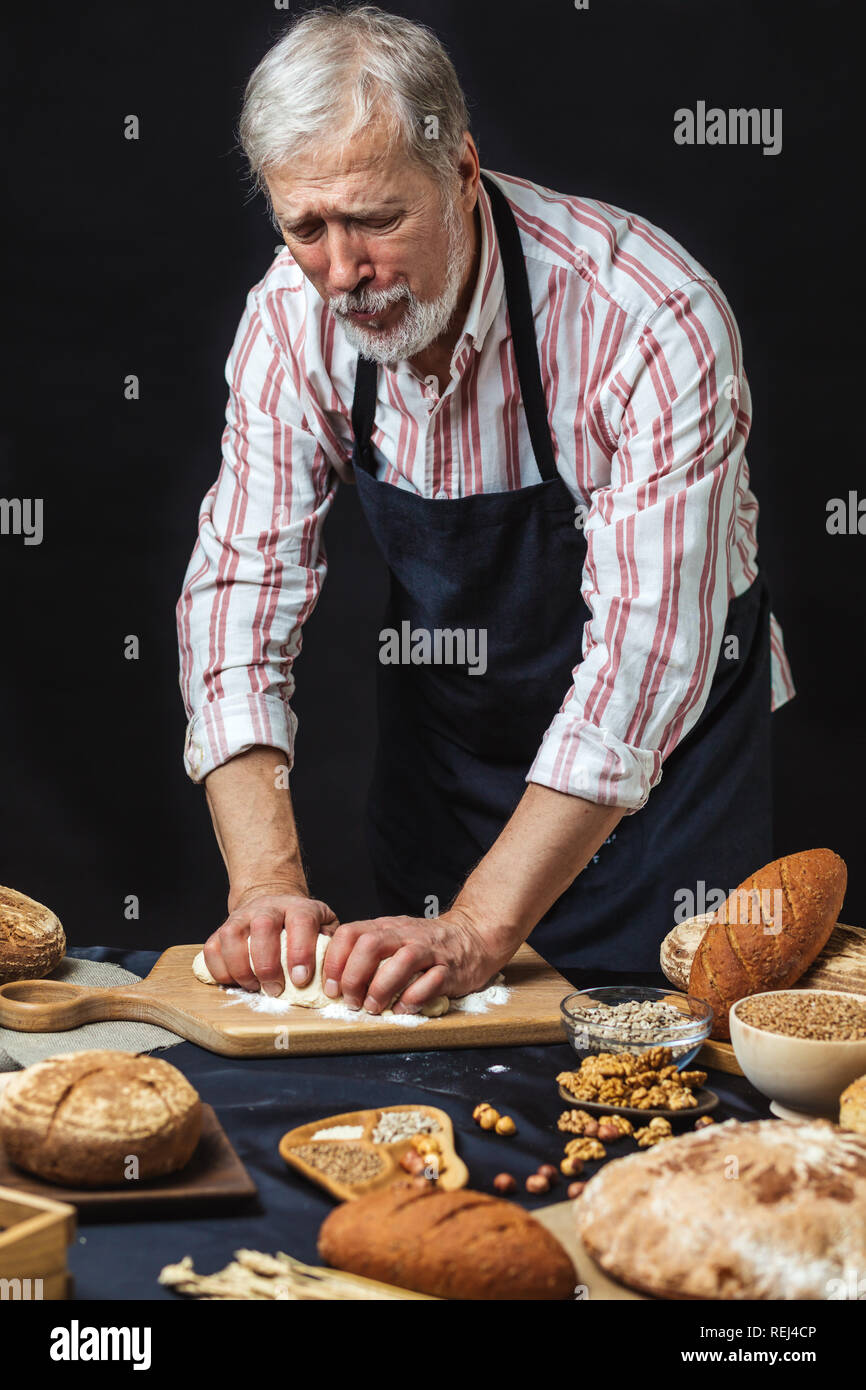 Mature bearded baker man kneading dough for bread on table Stock Photo