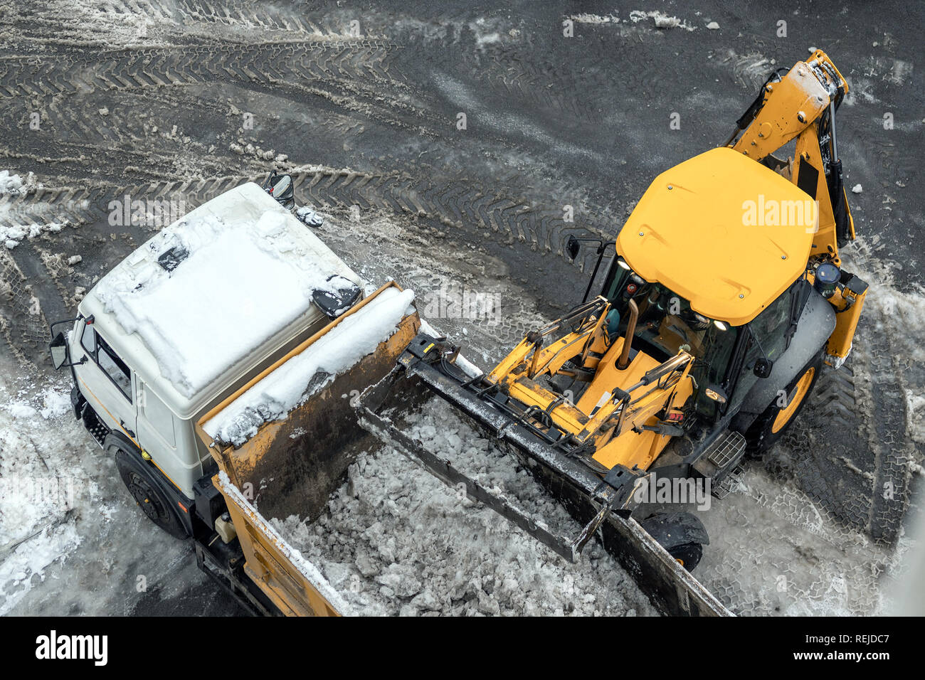Tractor loader machine uploading dirty snow into dump truck. Cleaning city street, removing snow and ice after heavy snowfalls and blizzard Stock Photo