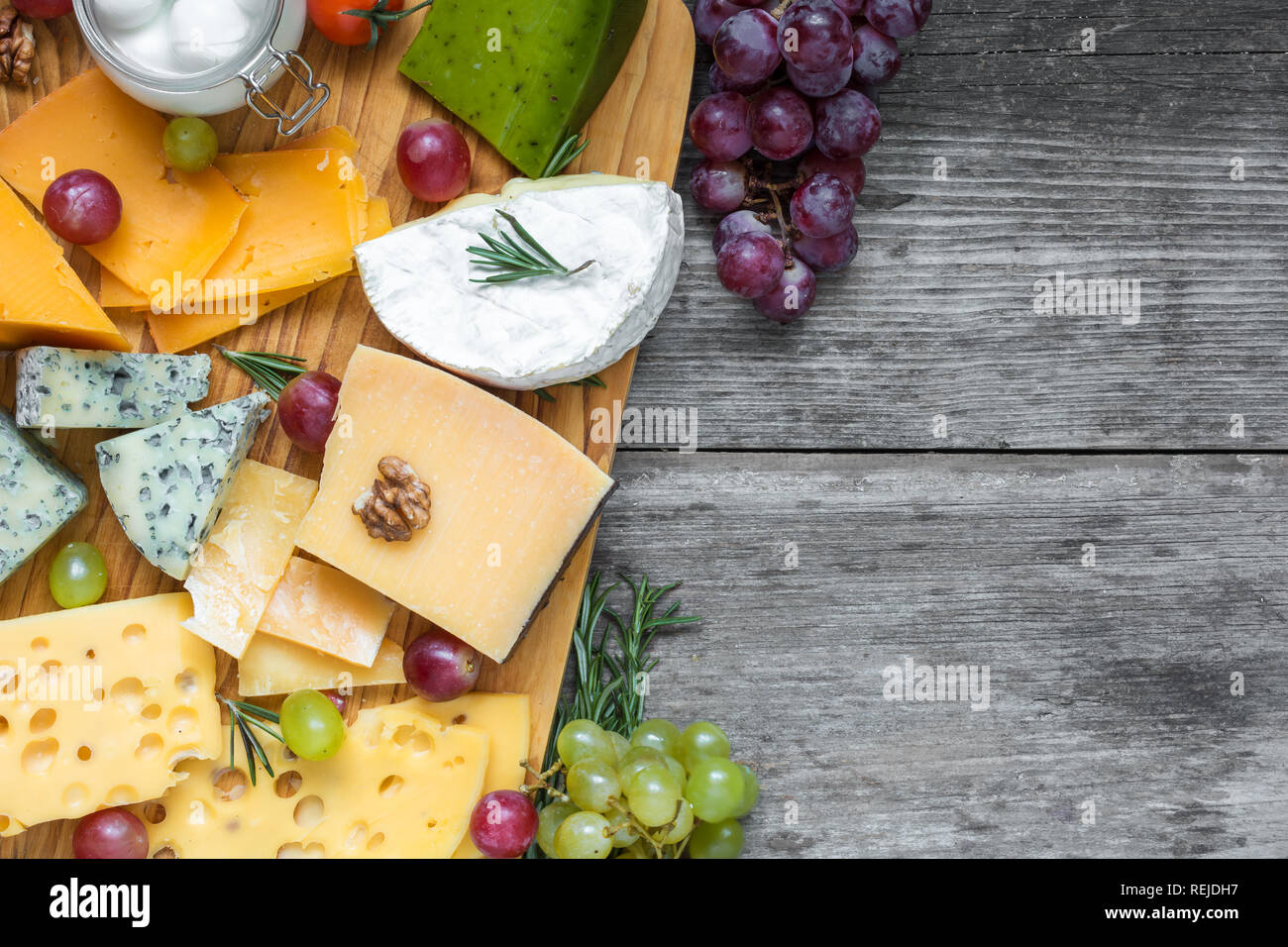 various types of cheese on cutting board with grape and nuts over rustic wooden table, top view with copy space Stock Photo