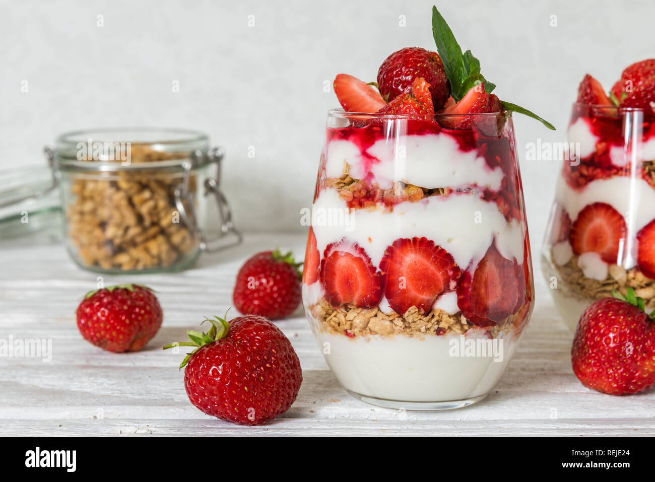homemade yogurt parfait with granola and strawberry in glasses on white wooden table. healthy breakfast Stock Photo