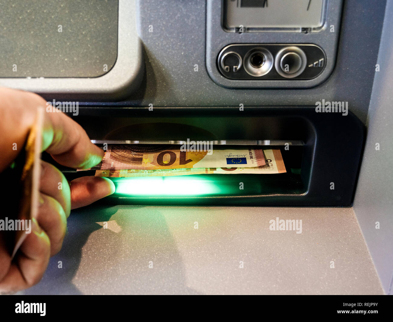 Close-up of an adult man's hand removing Euro cash money currency from slot of an automatic teller machine (ATM) Stock Photo