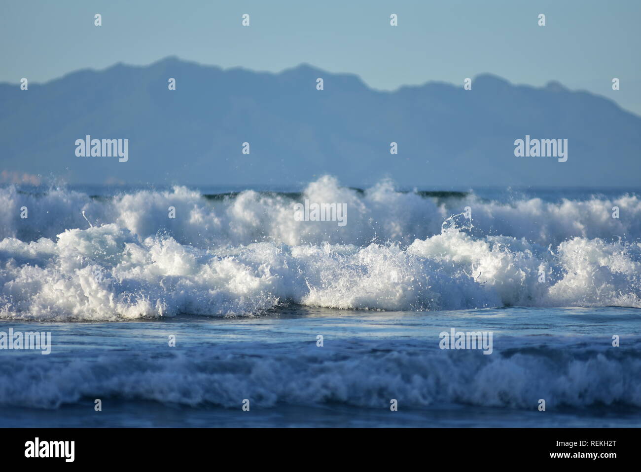 White foam of oceanic surf rolling towards camera with large landmass in distant background. Stock Photo