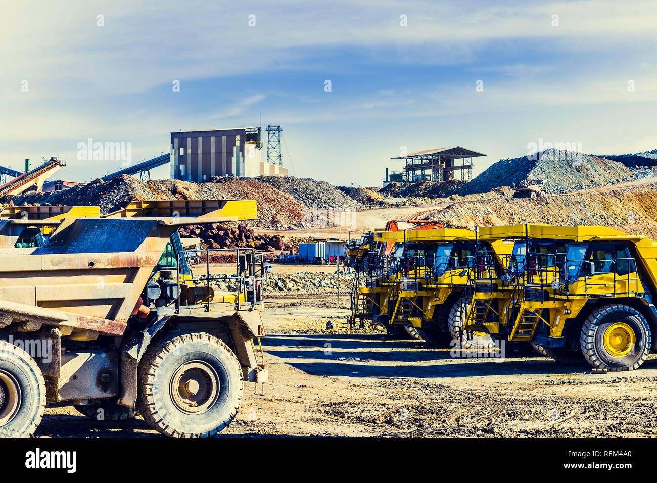 Old and new dumper trucks face to face in the Riotinto mine with old buildings in the background and truck loaded with ore going up the dirt road Stock Photo