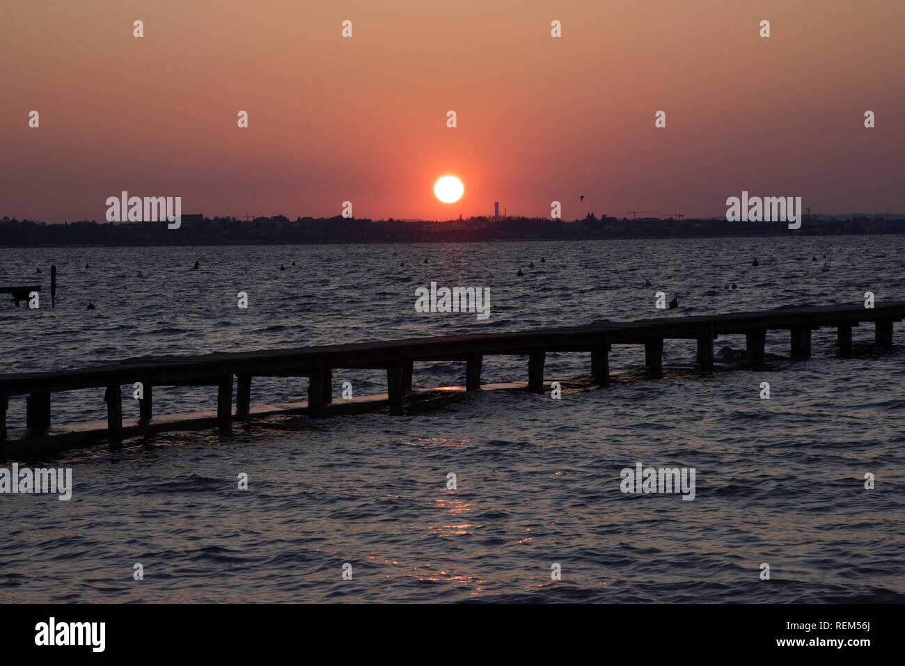 Sunset on the lake pier. Quiet tranquil lake at nature concept. Sun on the horizon, silhouette of bridge with sunset. Colorful sky with clouds Stock Photo