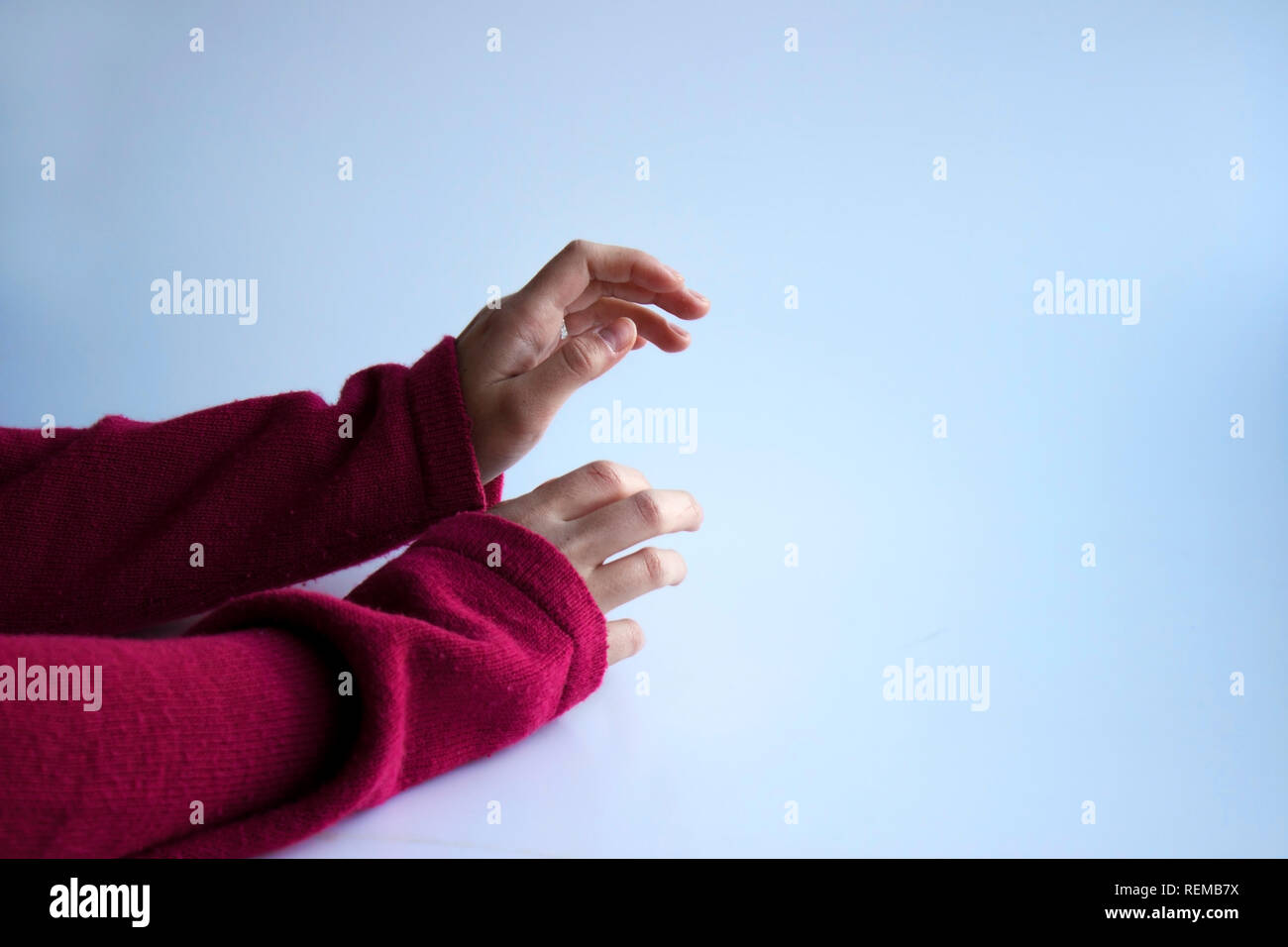 hands of a girl in a cozy purple magenta old sweater on a blue background Stock Photo