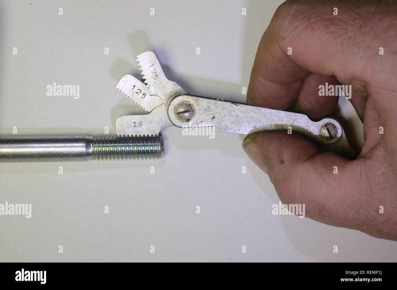 Determining the increase of a thread on a metric bolt. A pitch gauge is used, 1,25 mm and 1,75 mm blades will not fit, but 1,5mm will. Stock Photo