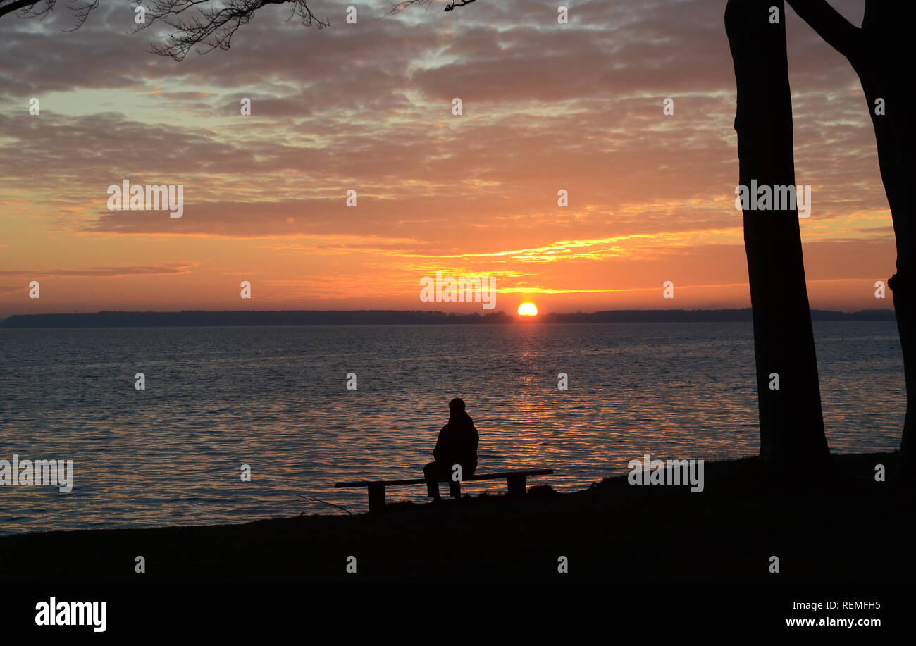Landscape with silhouette of a person sitting on a bench, sunset and altocumulus clouds over the sea.. Stock Photo