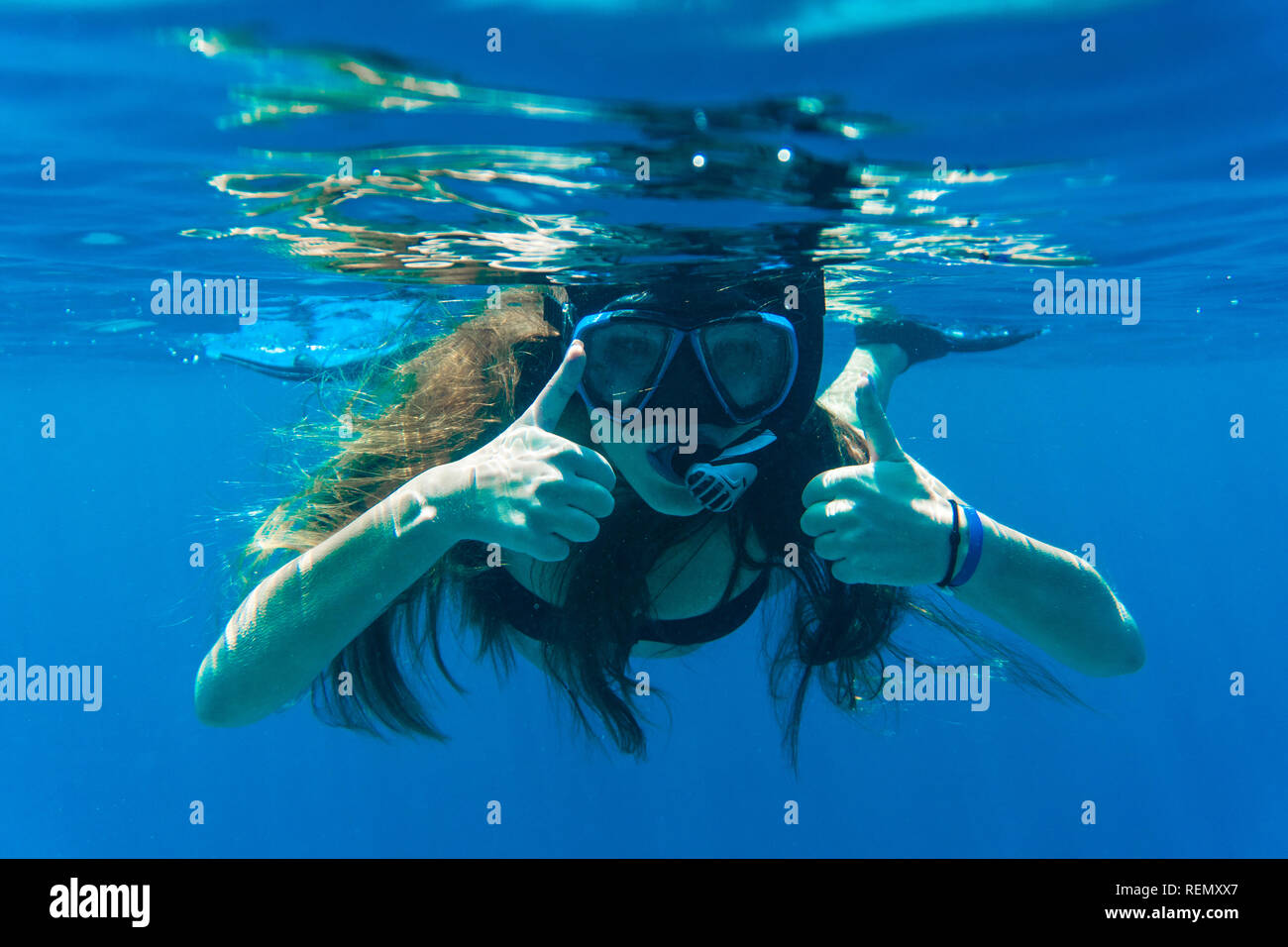 Young woman snorkeling making thumbs up signs underwater near coral