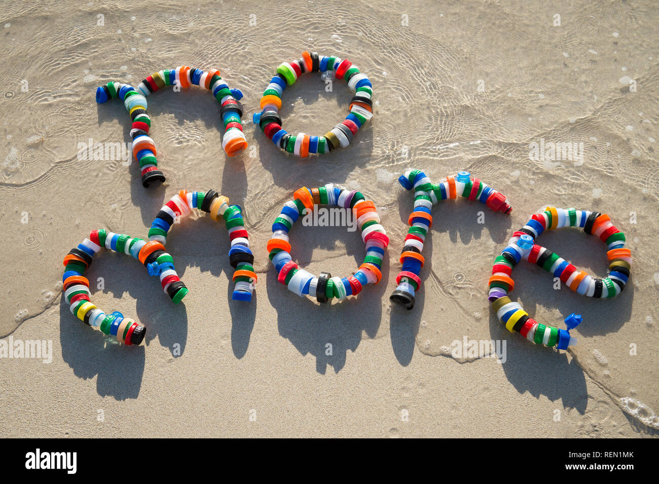No More message made from colorful used plastic bottle cap garbage on the smooth sand shore of a tropical beach Stock Photo