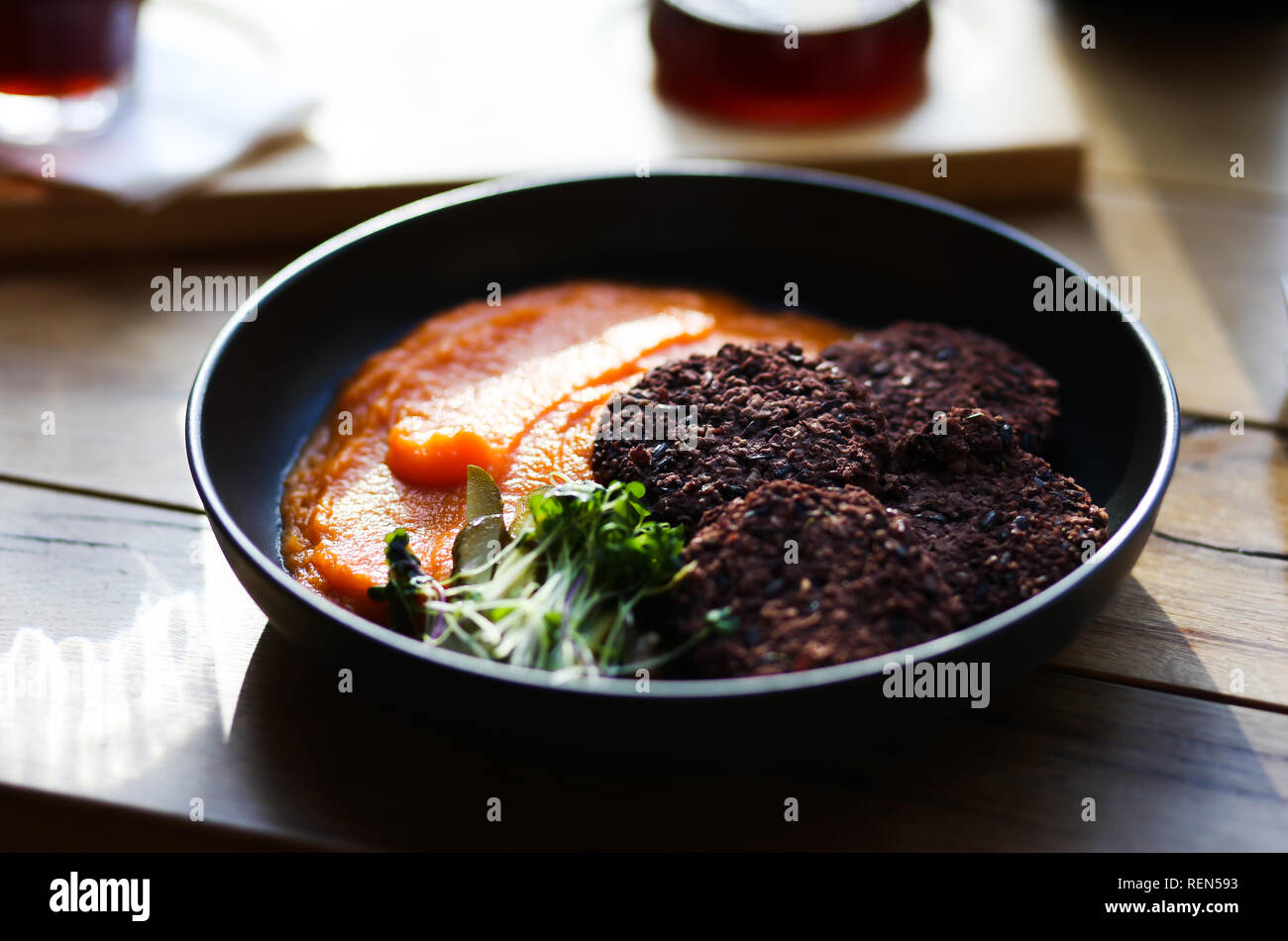 Vegan black rice cutlets served with orange carrots mesh and microgreeens and decaf coffee. Vegeterian food hipster cafe. Stock Photo