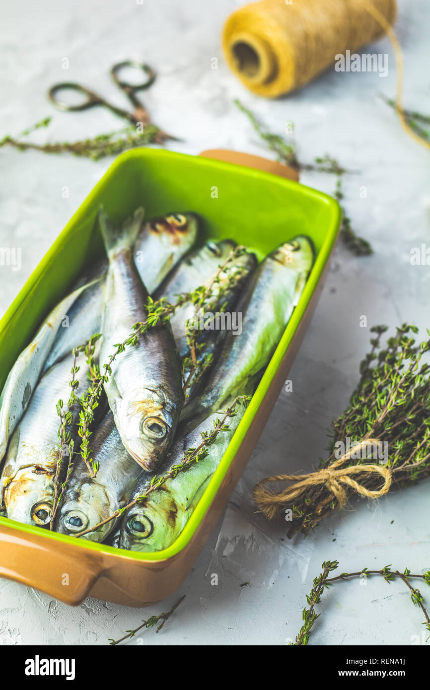 Sardines or baltic herring on green dish with thyme on light gray