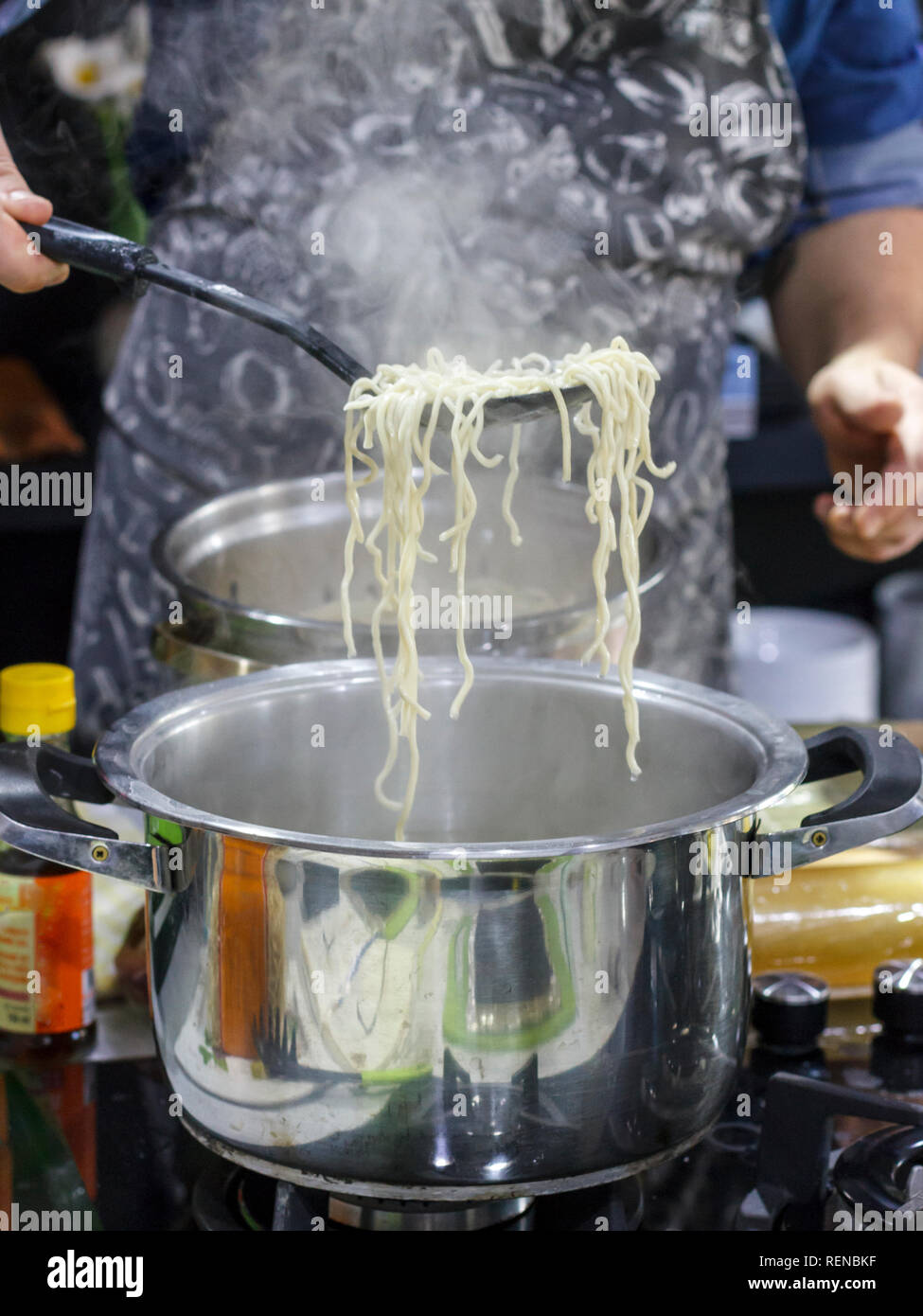 Chef takes out with slotted spoon hot steaming egg noodles from pan Stock Photo