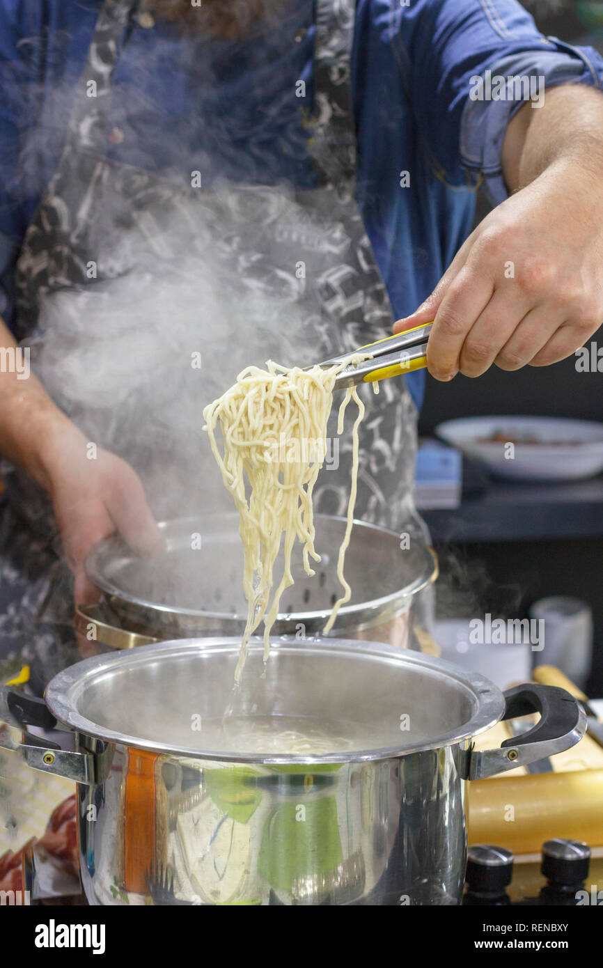 Chef takes out with slotted spoon hot steaming egg noodles from pan Stock Photo