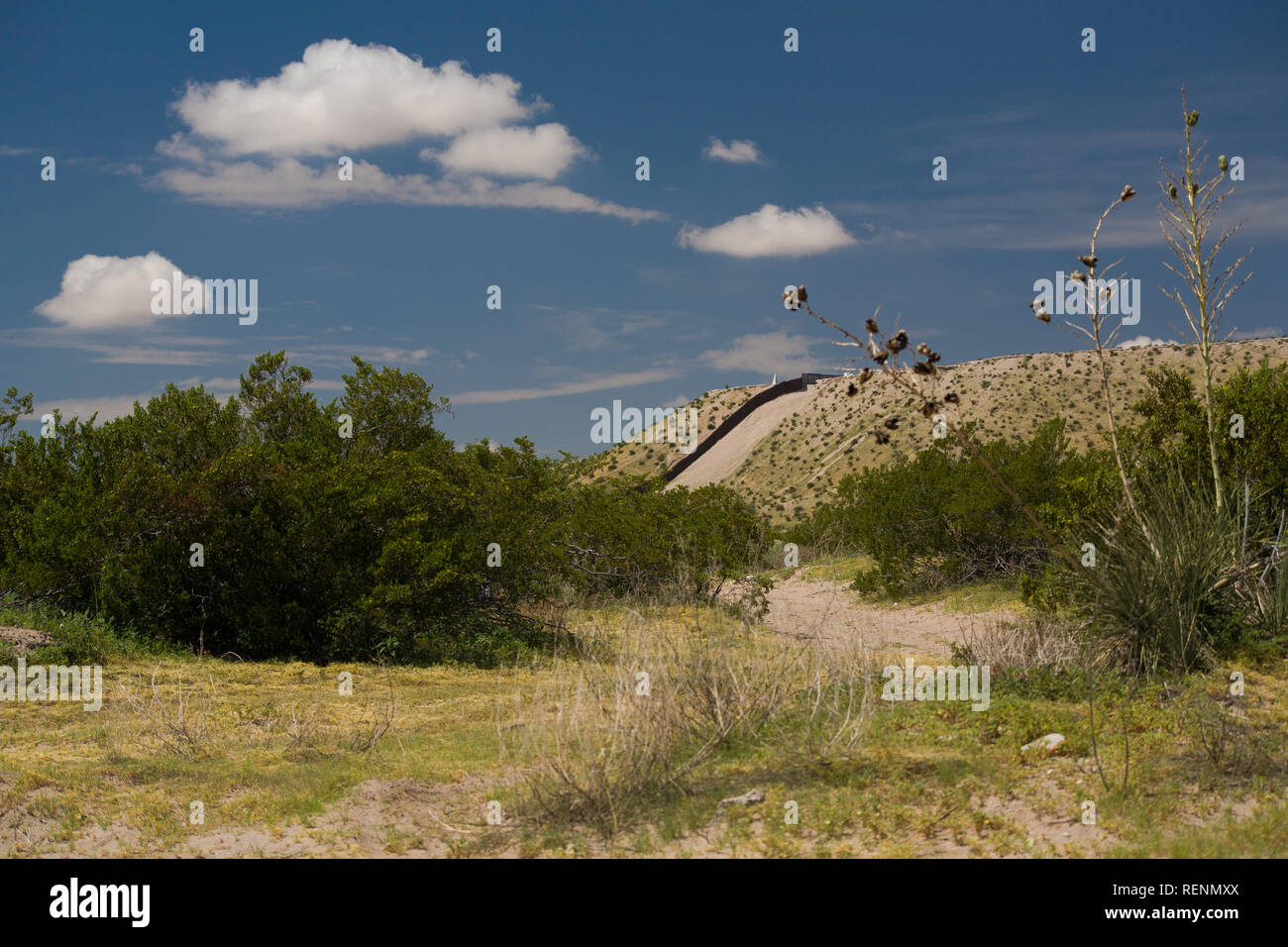 The US-Mexico Border Fence along a Steep Hill in Sunland Park, New Mexico near El Paso, Texas with Train Tracks in the Foreground Stock Photo
