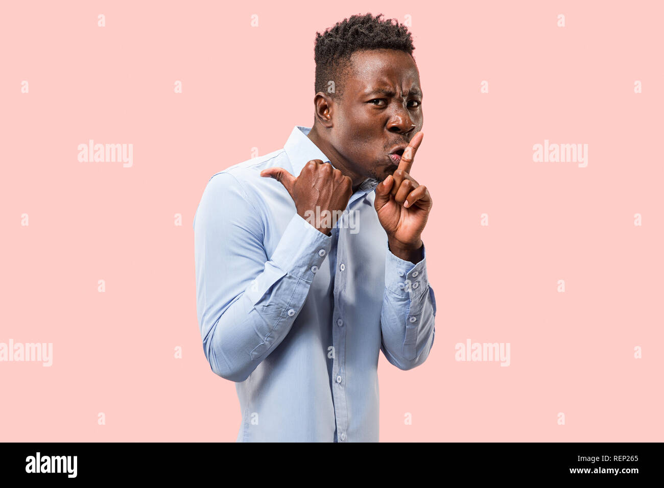 Secret, gossip concept. Young afro man whispering a secret behind his hand. Businessman isolated on trendy pink studio background. Young emotional man. Human emotions, facial expression concept. Stock Photo