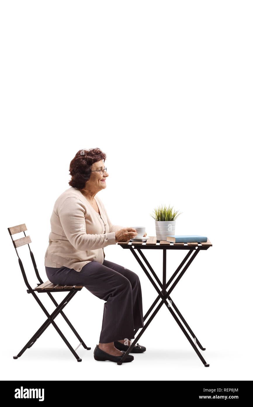 Full length profile shot of an elderly woman drinking coffee at a table alone isolated on white background Stock Photo