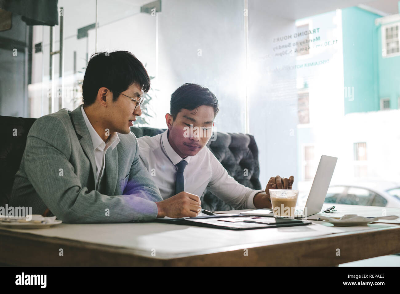 Two asian business men working together in a coffee shop. Business colleagues sitting at coffee shop table analysing some documents. Stock Photo