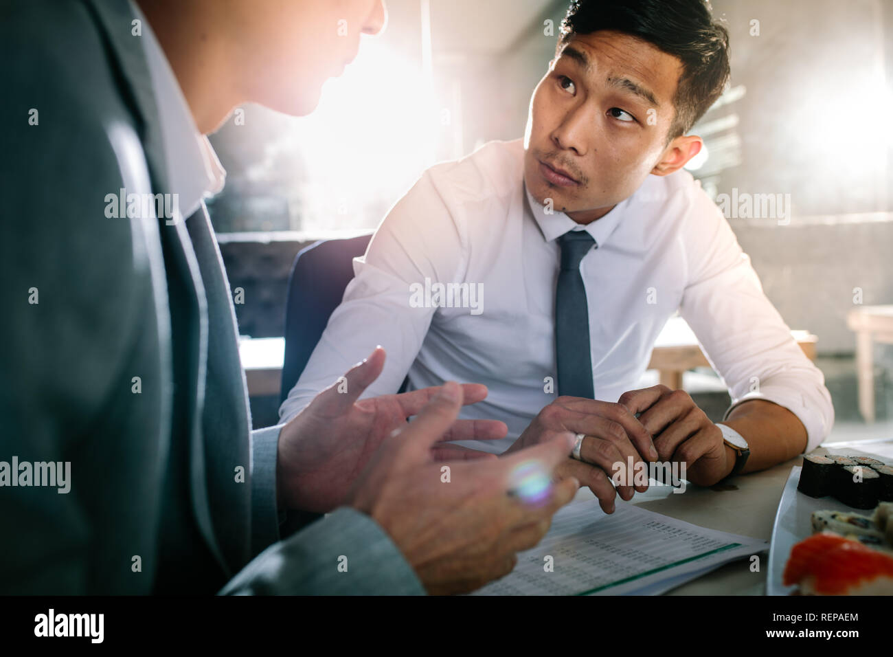 Young man listening to his colleague sitting at coffee shop. Two business people discussing over new project at a restaurant. Stock Photo