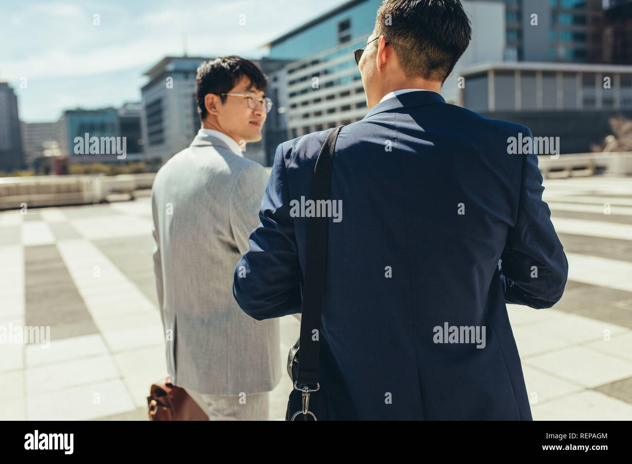 Rear view of two business people walking and talking together outdoors in the city. Two businessmen talking and walking in the city. Stock Photo