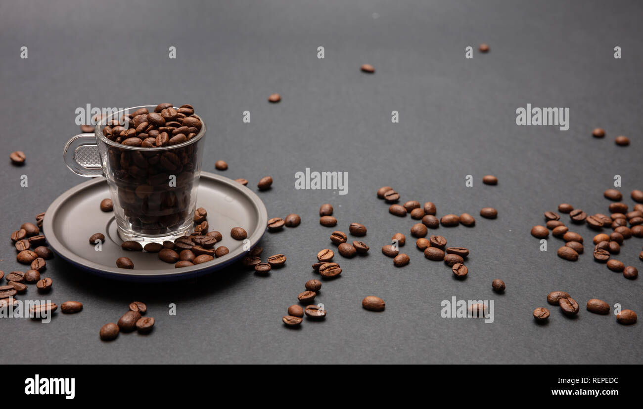 Coffee beans in a glass cup with sauser, on black background, copy space Stock Photo