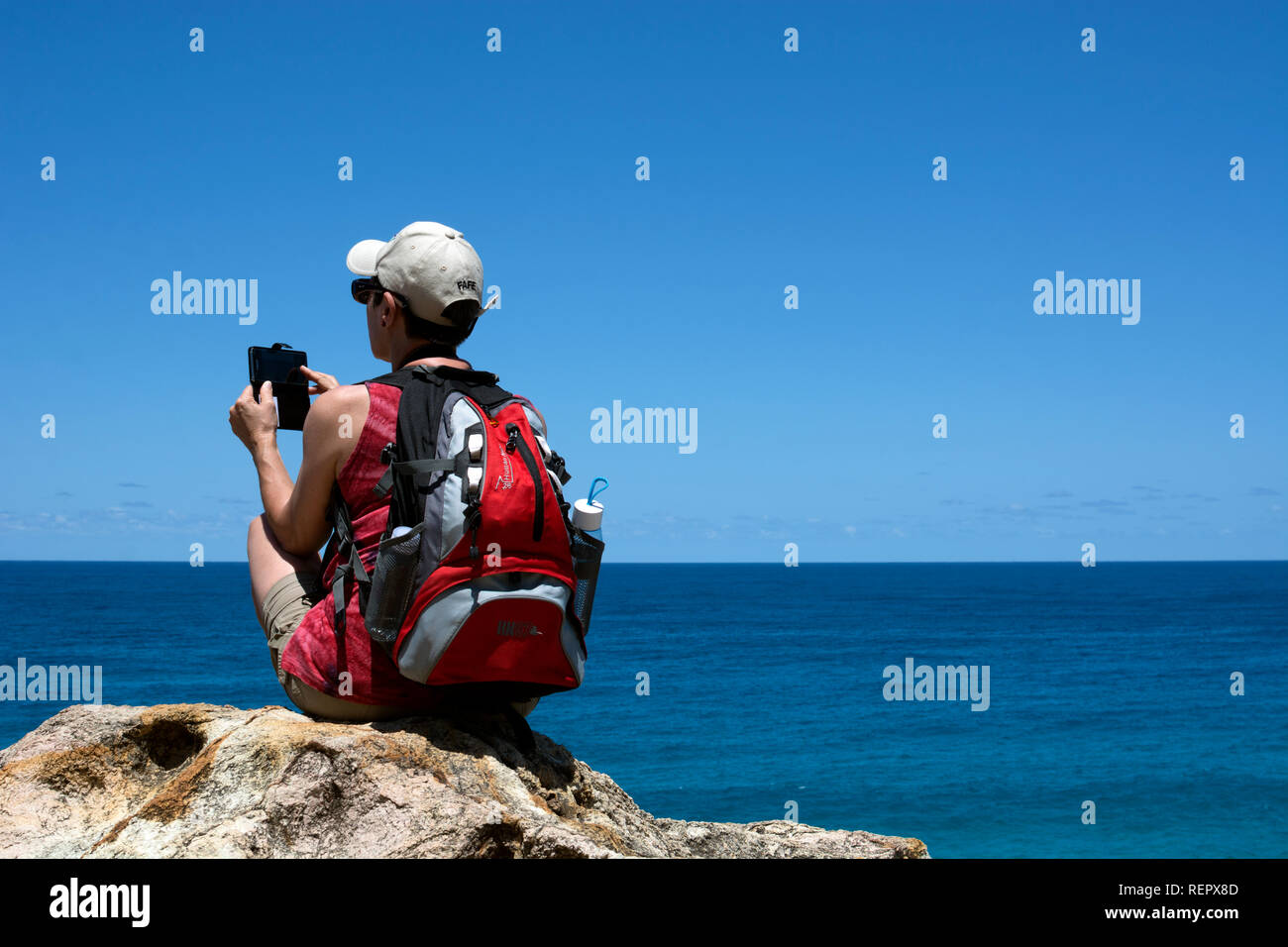 A young woman taking a photograph with a phone at North Gorge Walk, Point Lookout, North Stradbroke Island, Queensland, Australia Stock Photo