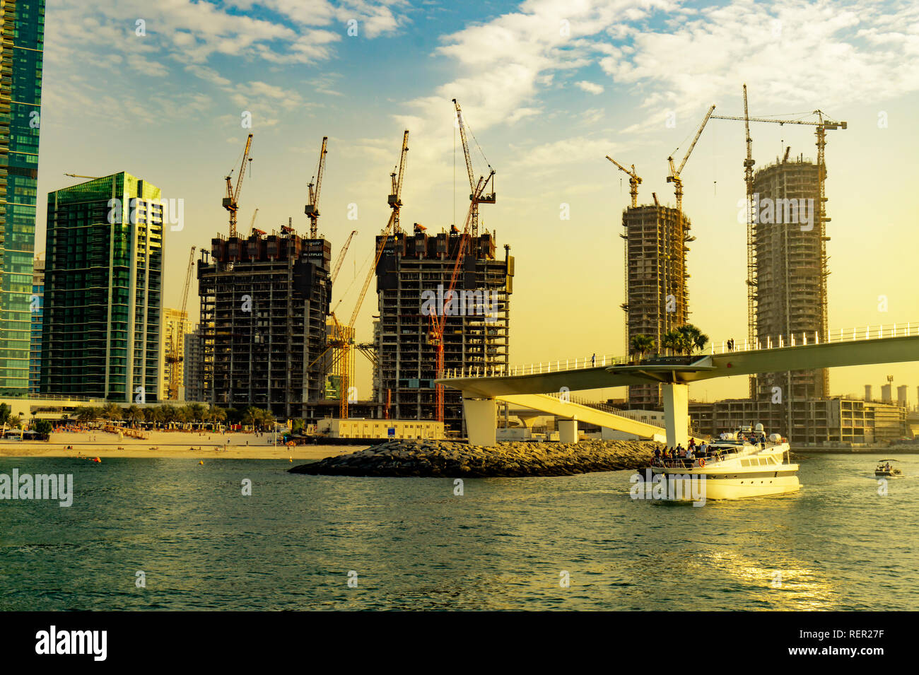 Dubai, UAE 11. 10. 2018 : Dubai contractions on the coast line with cranes everywere in sunset and a boat with tourists Stock Photo