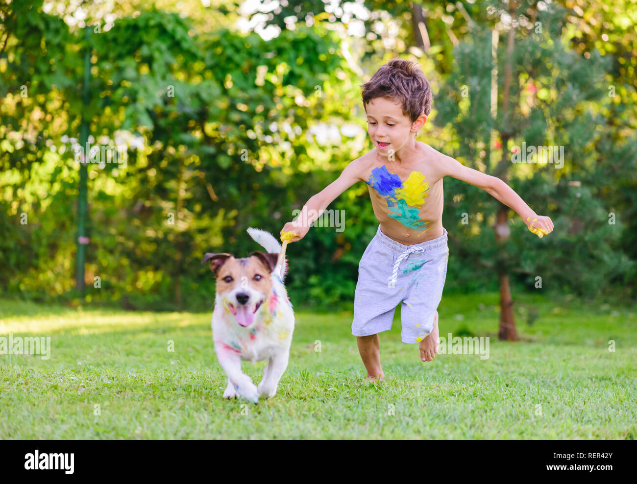 Naughty boy painting with brush on dog trying to escape Stock Photo
