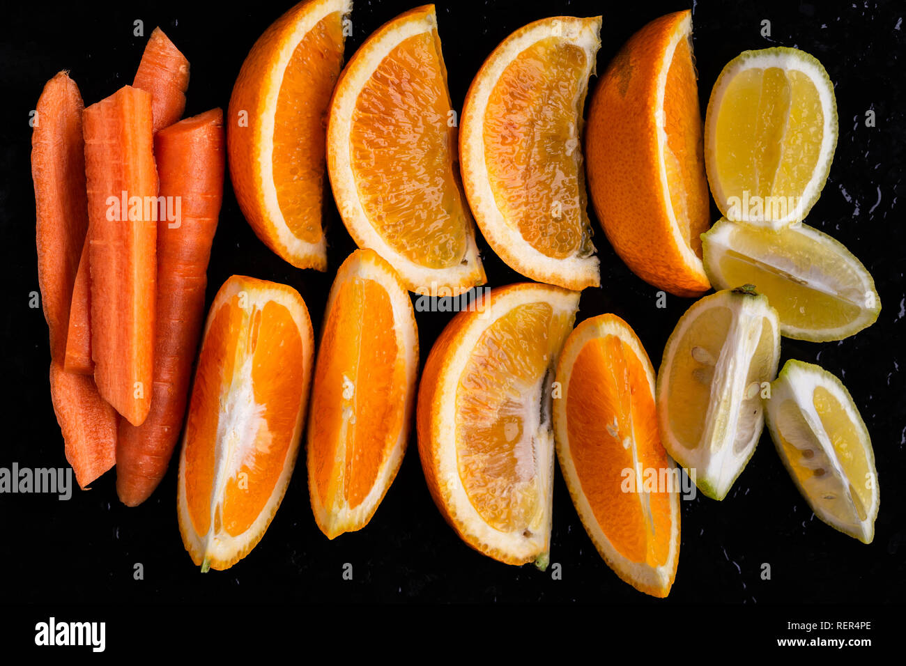 Directly above shot of slices of orange, lemon, carrots on black background Stock Photo