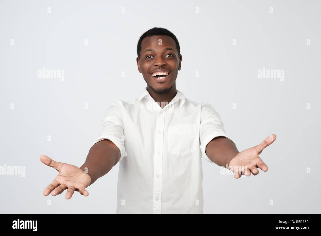 Cheerfull african man in white shirt, pulling hands towards camera, wanting to cuddle Stock Photo