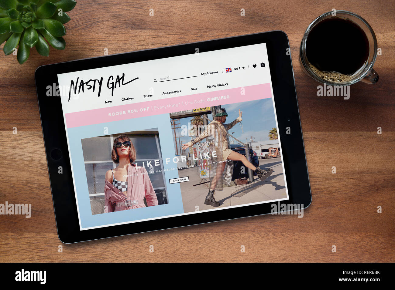 The website of Nasty Gal is seen on an iPad tablet, on a wooden table along with an espresso coffee and a house plant (Editorial use only). Stock Photo