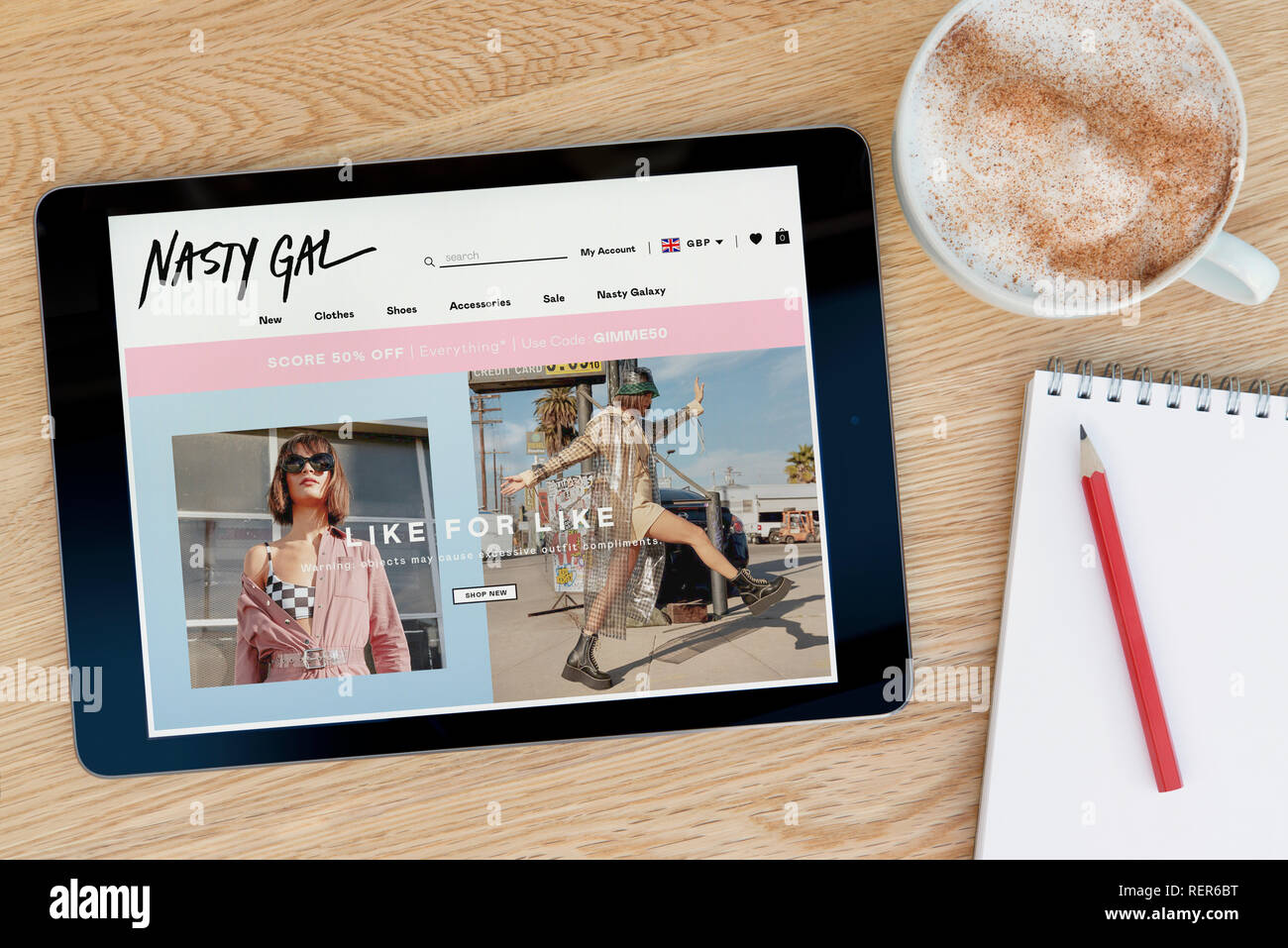 The Nasty Gal website features on an iPad tablet device which rests on a wooden table beside a notepad and pencil and a cup of coffee (Editorial only) Stock Photo