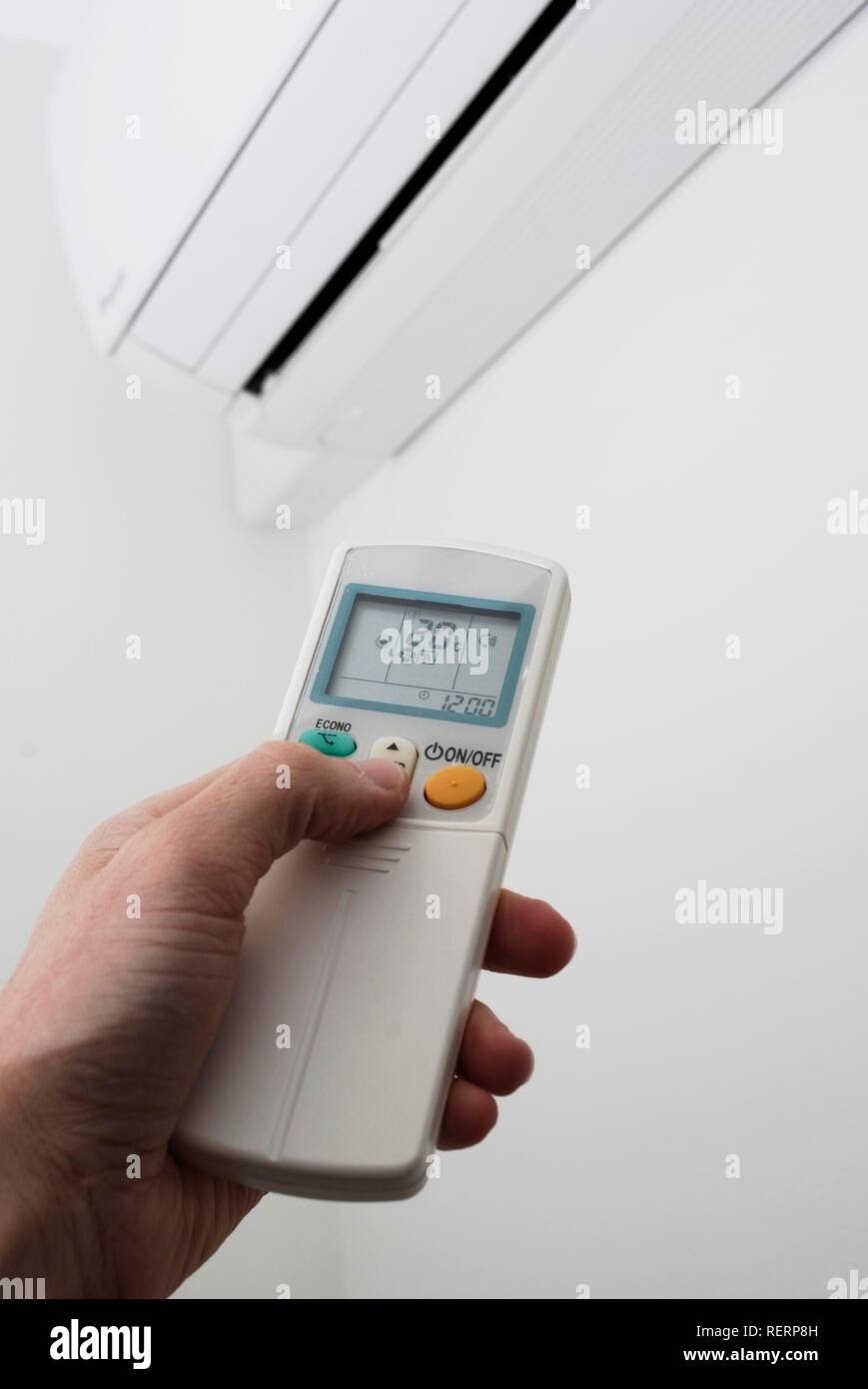 Hand adjusting the settings of a wall-mounted air conditioning unit with remote control Stock Photo