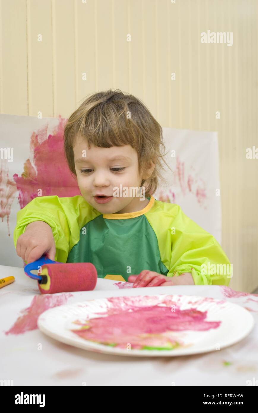 A two year old girl in a plastic smock painting in a playroom with a