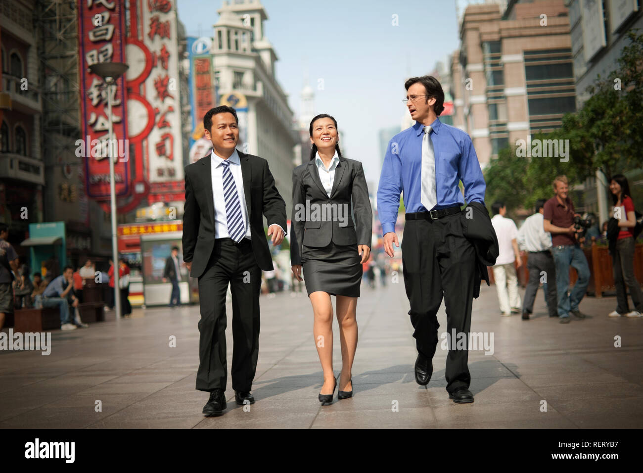 Three business colleagues walking down a busy street while talking. Stock Photo