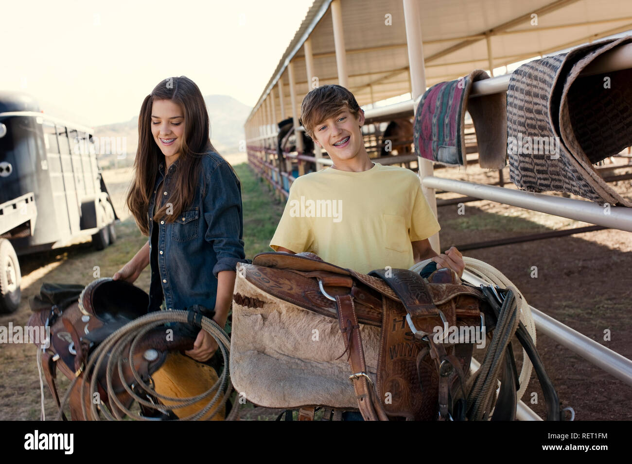 Portrait of two smiling teenagers holding horse riding saddles. Stock Photo