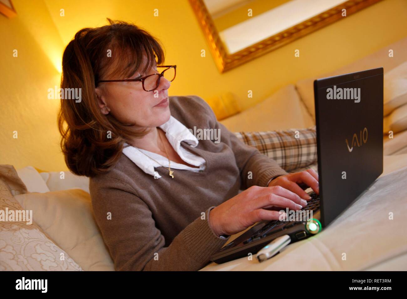 Woman, 45 years old, surfing the internet with a laptop on a sofa, DSL-stick, mobile internet Stock Photo