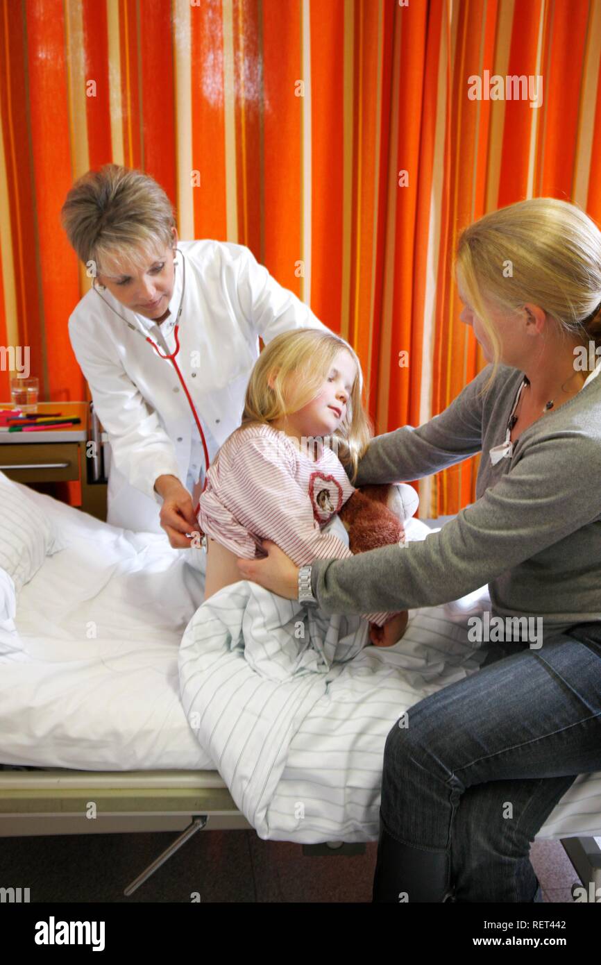 Doctor examining a young patient, seven years old, supported by the mother, at the bedside in a hospital Stock Photo