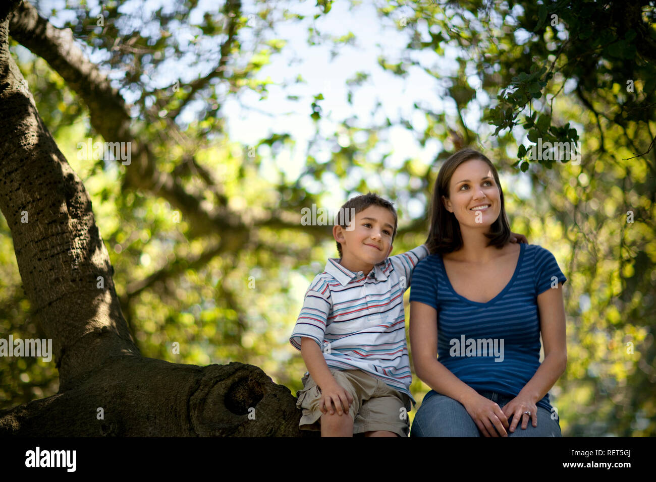 Happy mother and son sitting on a tree branch. Stock Photo